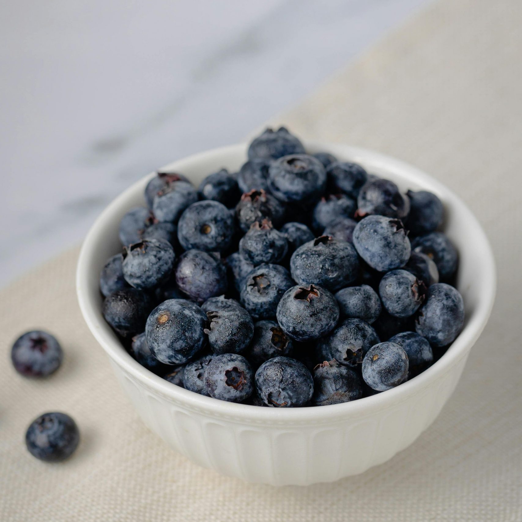 A delicious bowl of fresh, juicy blueberries on a light background, perfect for healthy eating concepts.