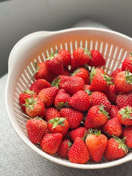 A vibrant collection of fresh strawberries in a white colander, perfect for food themes.