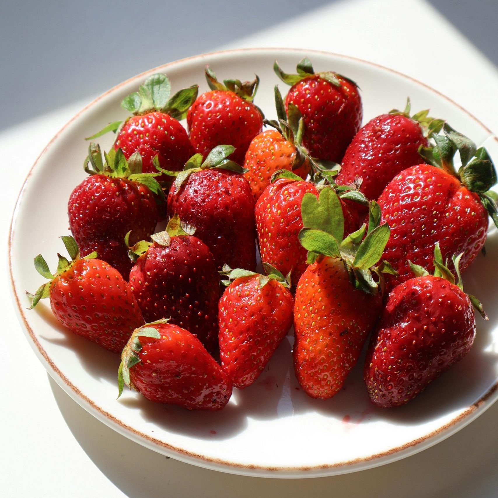 A plate of fresh strawberries bathed in sunlight, showcasing their vibrant red color.
